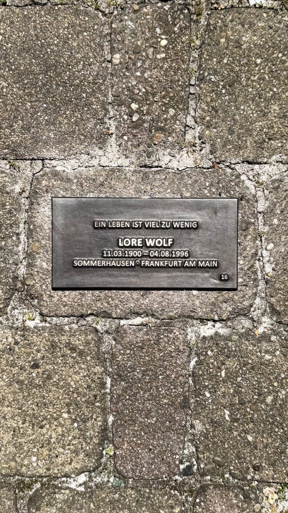 Bodenplatte zur Erinnerung an Lore Wolf mit Lebensdaten und dem Zitat „Ein Leben ist viel zu wenig“.
