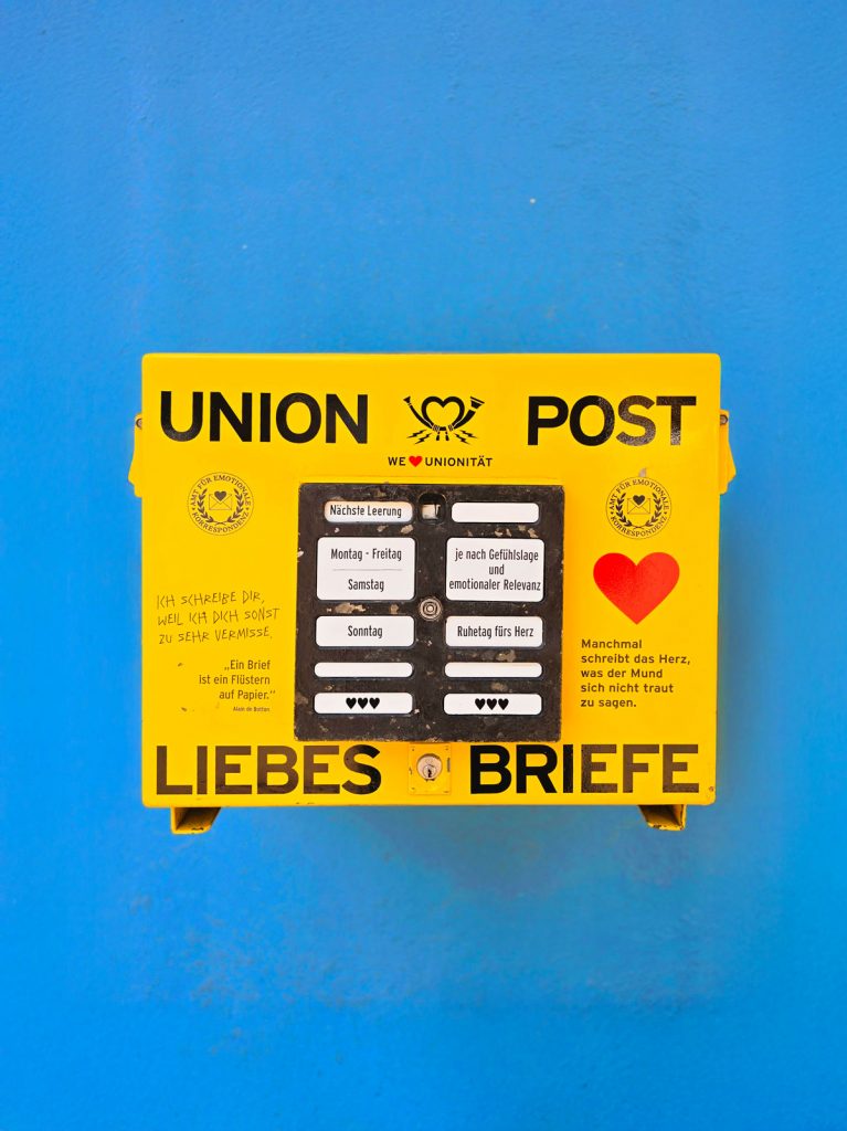 Gelber Briefkasten mit der Aufschrift „Union Post – Liebesbriefe“ vor blauer Wand, gestaltet für emotionale Botschaften.
