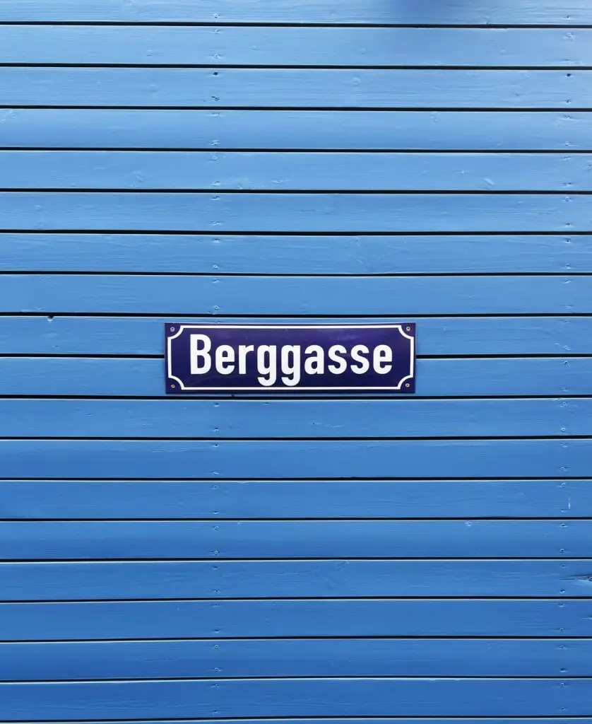 Straßenschild „Berggasse“ auf blauer Holzverkleidung mit waagerechter Lattenstruktur.