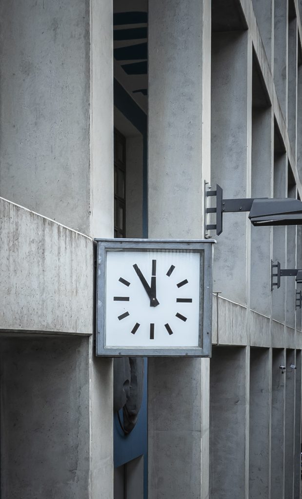 Wanduhr mit schlichten Balkenanzeigen zeigt fünf vor zwölf, montiert an Betonfassade des Union-Gebäudes.