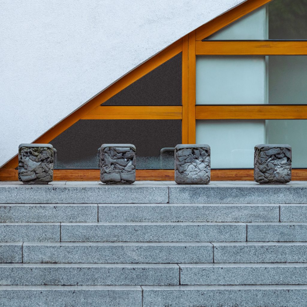 Vier Sitzquader mit unregelmäßiger Oberfläche auf Treppenstufe vor Glasfassade mit Holzrahmen.