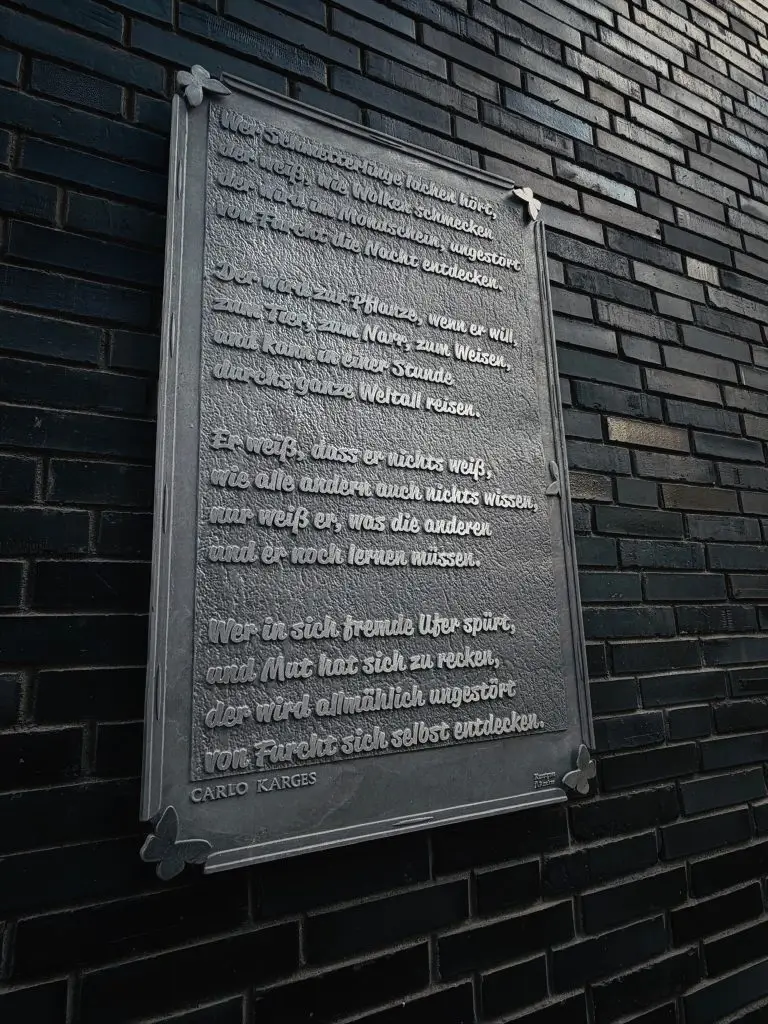 Metalltafel an Backsteinwand mit Carlo-Karges-Gedicht "Wer Schmetterlinge lachen hört", Union-Gelände Frankfurt.