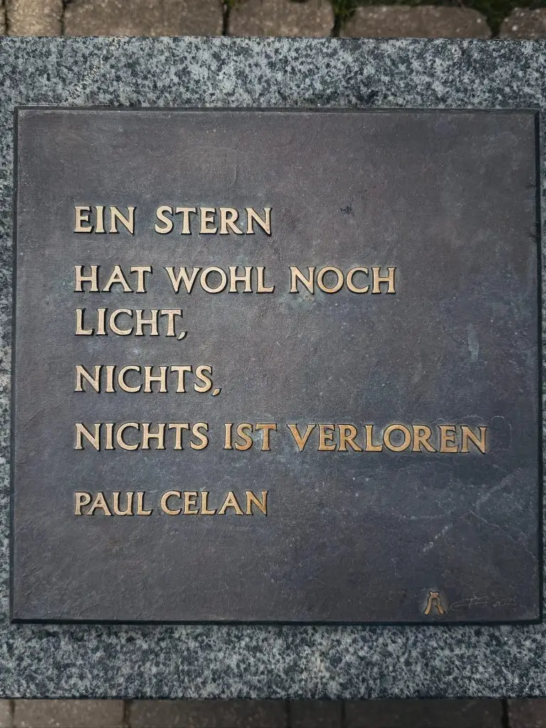 Nahaufnahme von Bronzetafel auf Steinsockel mit Zitat von Paul Celan ("Ein Stern hat wohl noch Licht...").