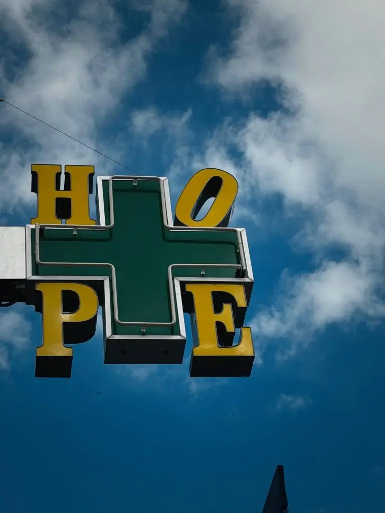 Grünes Kreuz und gelbe Buchstaben "HOPE" vor blauem Himmel.