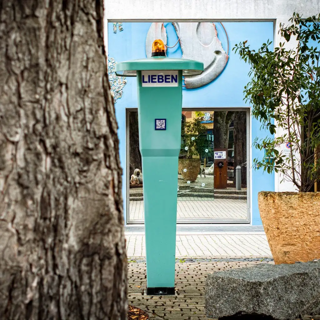 Türkisfarbene Notrufsäule mit der Aufschrift "LIEBEN" und QR-Code auf dem Union-Gelände in Frankfurt.