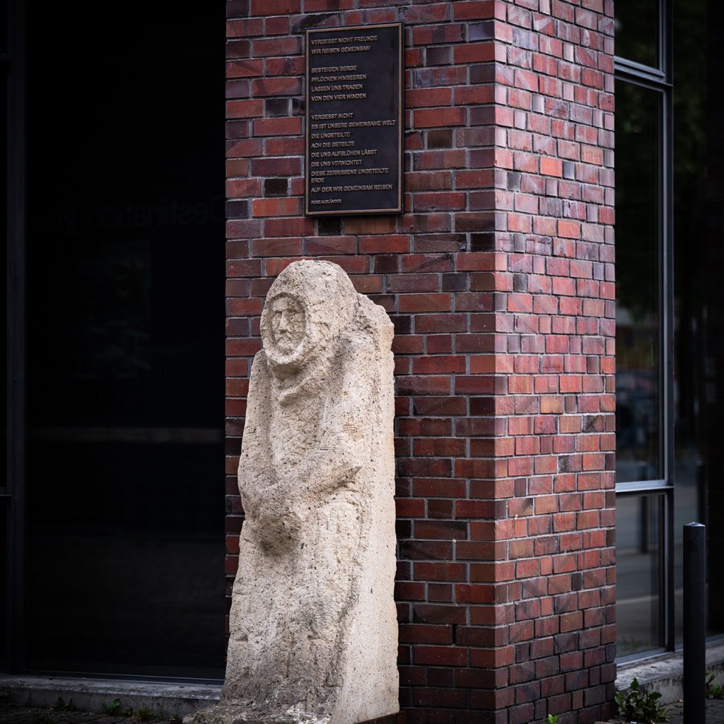 Verhüllte Steinskulptur unter einer Rose-Ausländer-Gedenktafel an roter Backsteinwand, Union-Gelände Frankfurt.