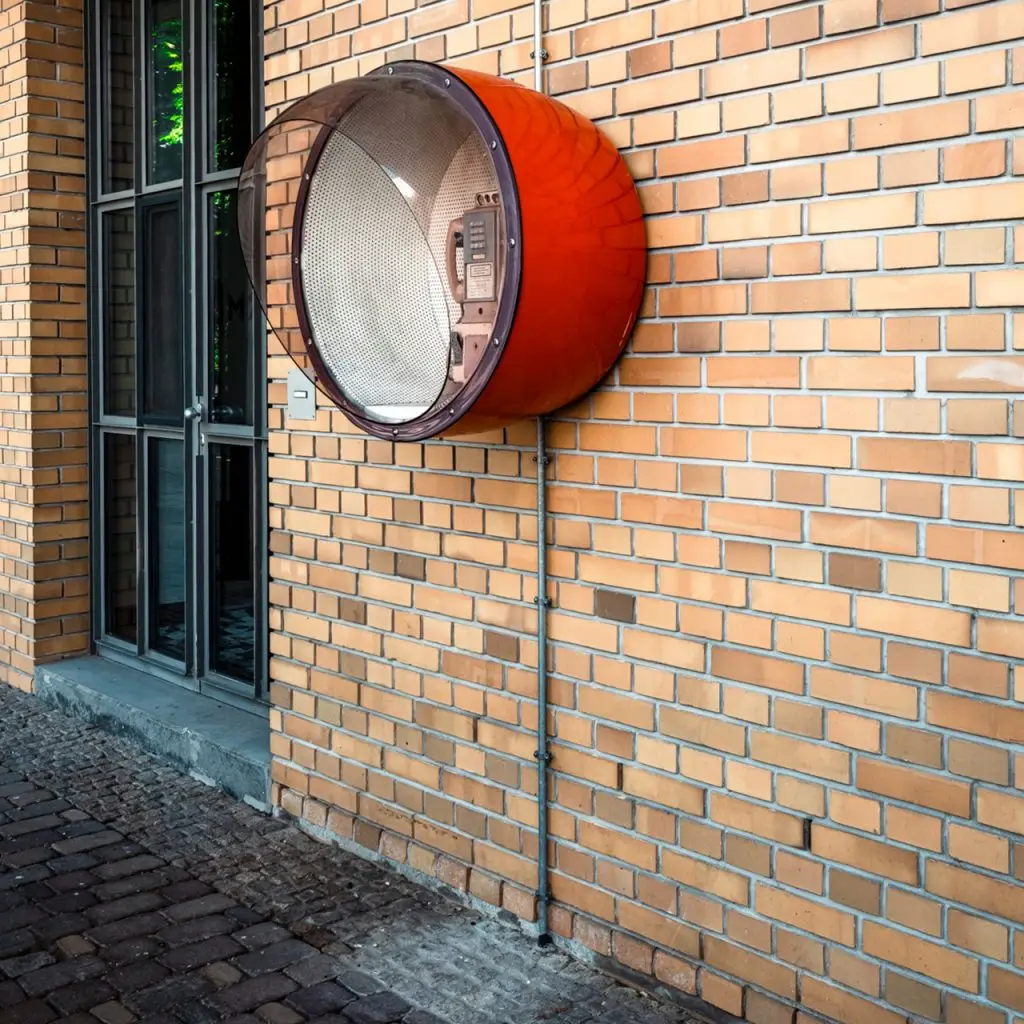 Orangefarbene Telefonhaube an einer Backsteinwand neben einer Glastür auf dem Union-Gelände in Frankfurt.