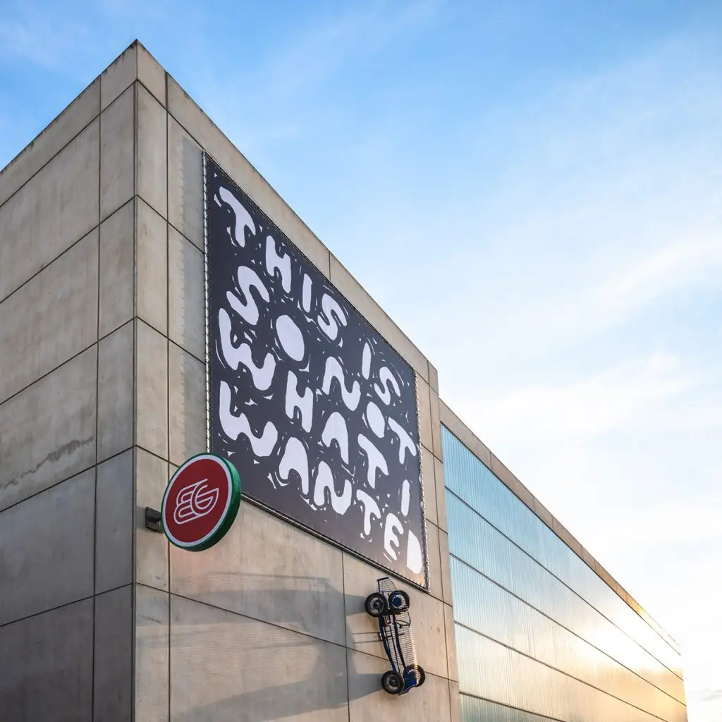 Kunstwerk von Stefan Marx mit 'THIS IS SO NOT WHAT I WANTED' Banner und Sportwagen-Skulptur, Weitwinkel.