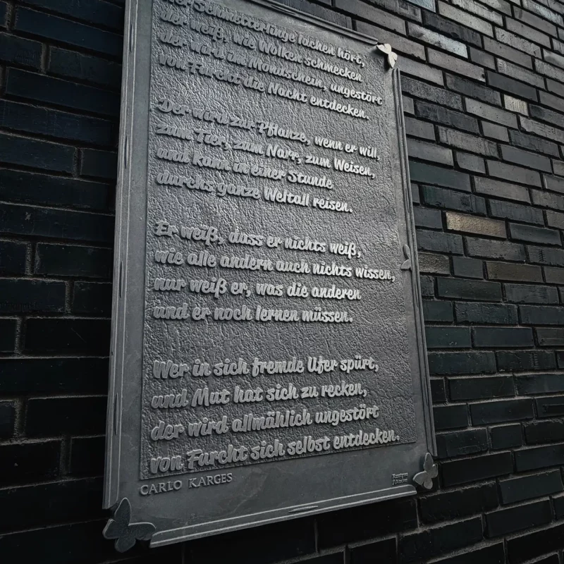 Metalltafel an Backsteinwand mit Carlo-Karges-Gedicht "Wer Schmetterlinge lachen hört", Union-Gelände Frankfurt.