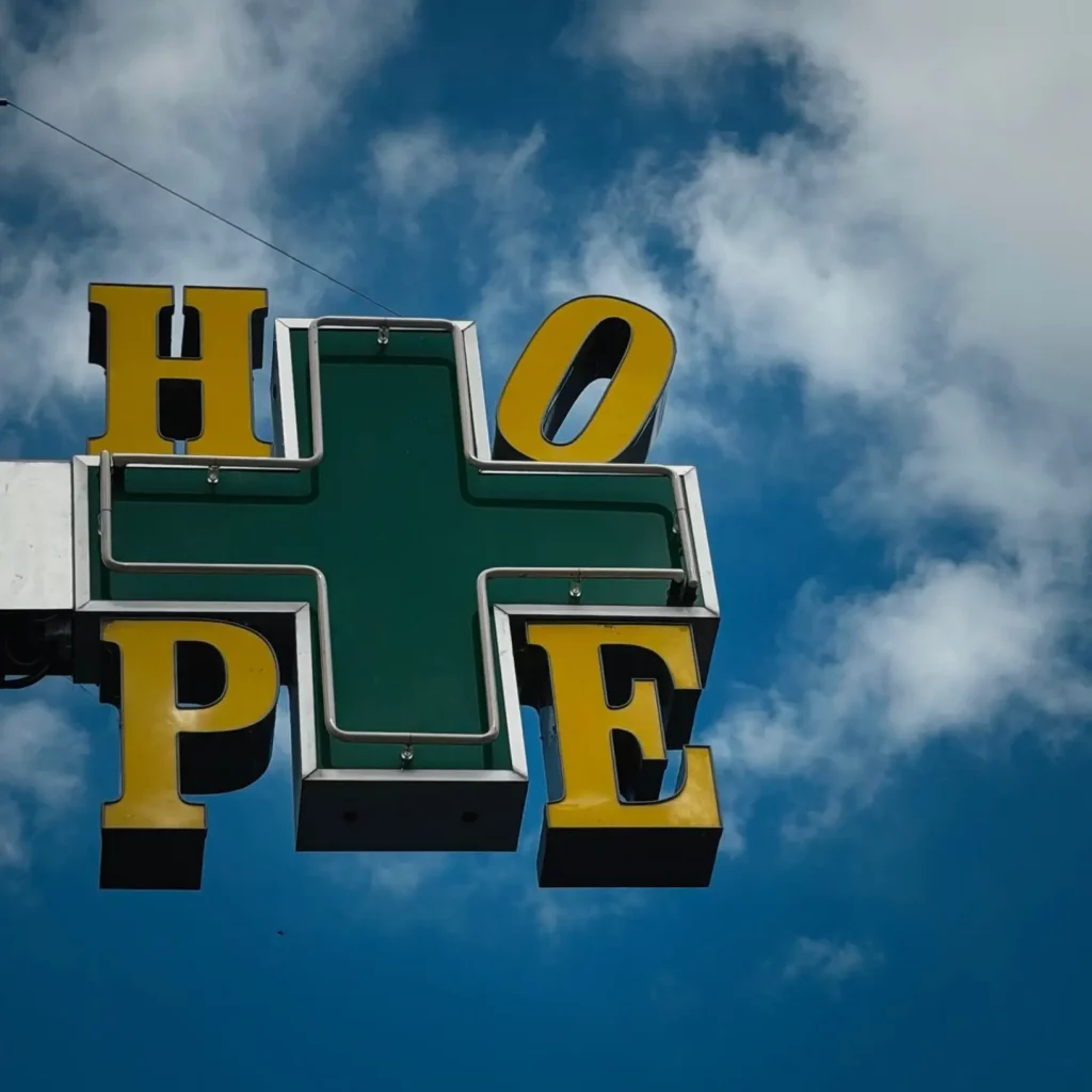 Grünes Kreuz und gelbe Buchstaben "HOPE" vor blauem Himmel.