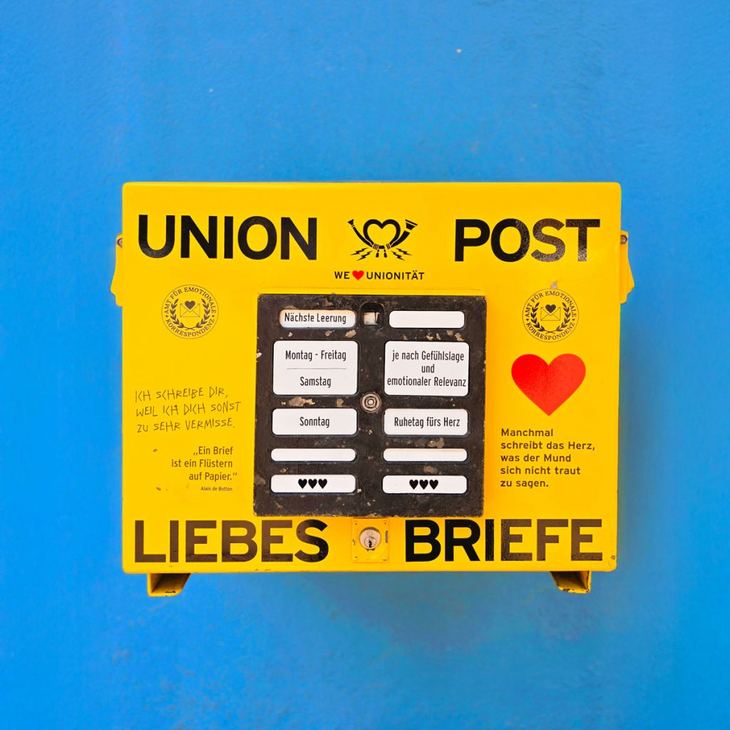 Gelber Briefkasten mit der Aufschrift „Union Post – Liebesbriefe“ vor blauer Wand, gestaltet für emotionale Botschaften.